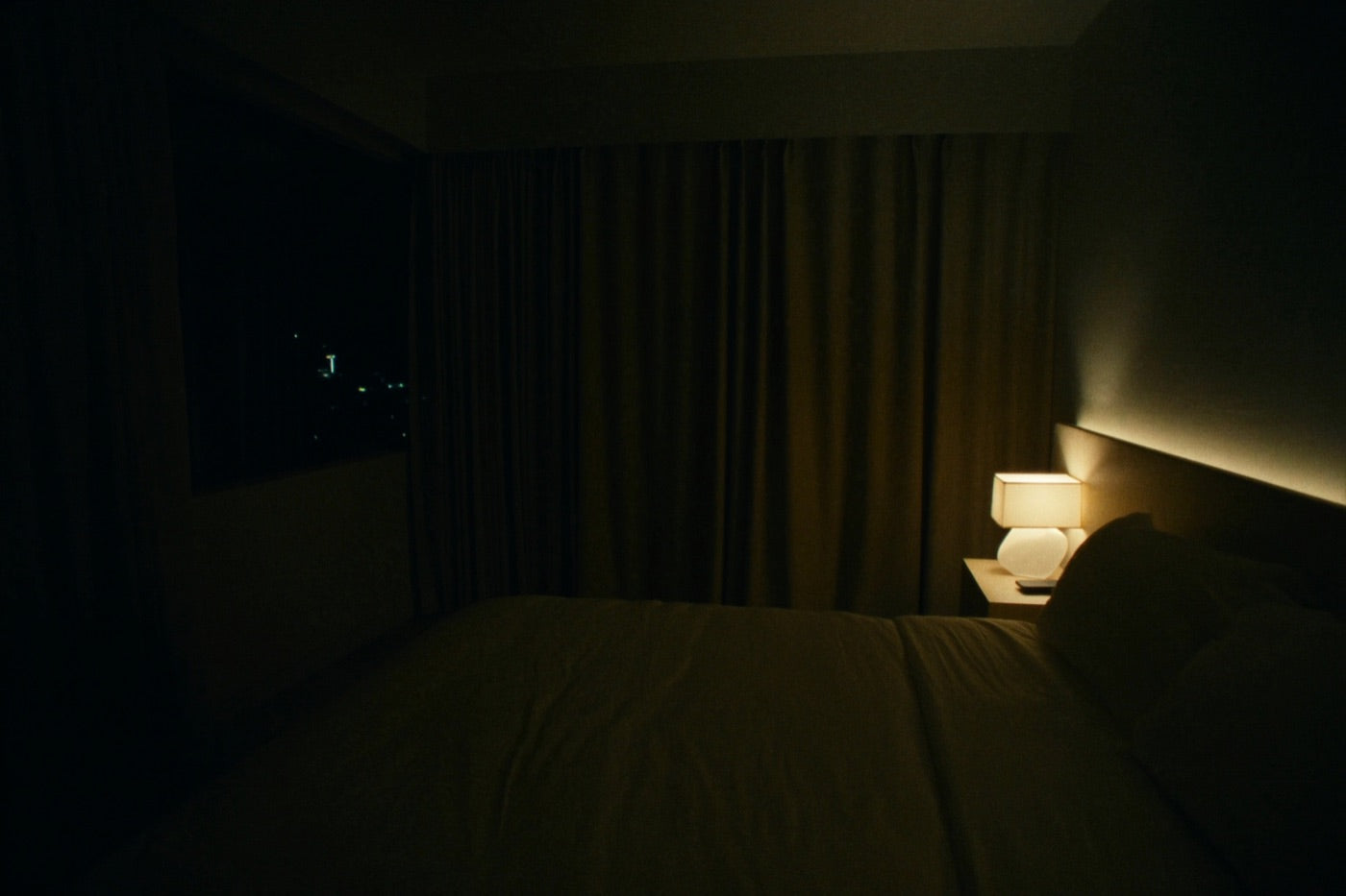 Dark bedroom lit only by a single warm bedside lamp